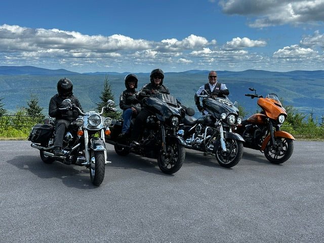 Four motorcycles and riders gathered at a mountain overlook under a blue sky