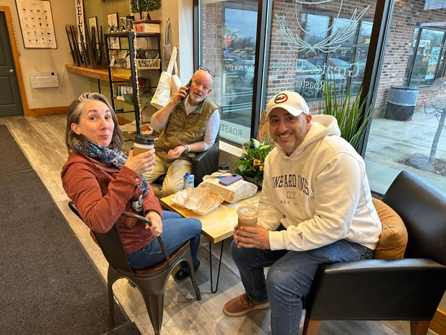 Three people smiling and sharing drinks around a table inside the café
