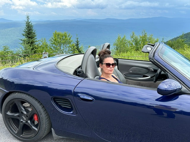 Jill behind the wheel of a convertible with mountain views behind her