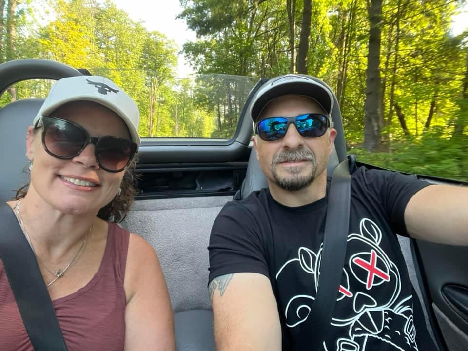 A smiling couple in a convertible on a tree-lined road