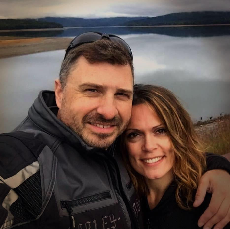 Ray and Jill smiling at a lakeside stop with mountains in the background
